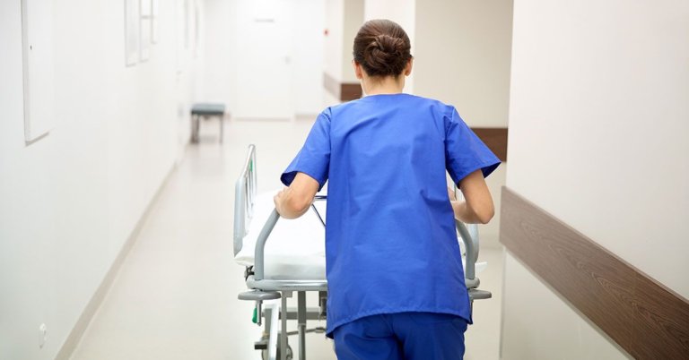 A nurse in blue overalls pushing a stretcher in a hospital